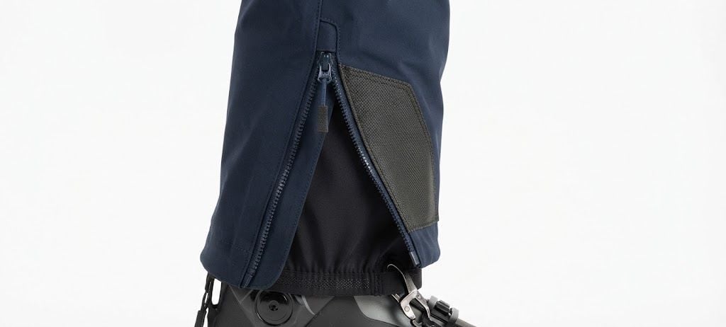 Bajo de un pantalón con la cremallera abierta: la polaina interior elástica ajustada sobre la bota y el refuerzo anti-canto en la cara interna del tobillo